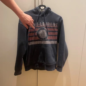 Mörkblå Saint Laurent hoodie - Snygg mörkblå hoodie från Saint Laurent med tryckt logga och emblem på bröstet. Hoodien har en klassisk känguruficka, justerbar huva med snören och ribbade muddar. Perfekt för en avslappnad och trendig look.