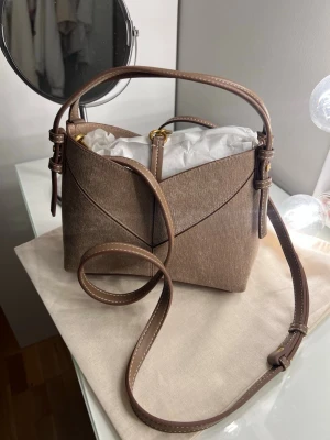 Mini shoppingväska med sömmar - Handväska från Zara i beige mocka-look med mjuk, trekantig form och justerbara remmar i matchande färg. Väskan har ett kort handtag och en lång axelrem för olika bärstilar. Snygga sömdetaljer❣️ Aldrig använd endast testad, pris kan diskuteras! (Inte under 300kr då nypris är 379)