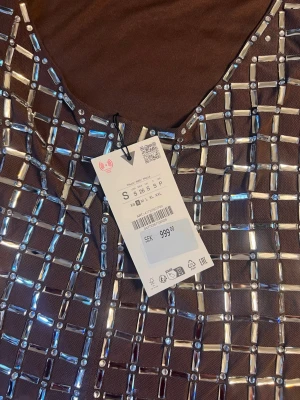 Brun kort klänning med paljetter - Supersnygg brun kort klänning med tunna axelband och ett rutigt mönster av silvriga paljetter. Klänningen har en figurnära passform och är perfekt för dig som vill sticka ut. Materialet känns mjukt och stretchigt, vilket gör den bekväm att bära hela kvällen.OBS! Ingen retur 🔊🔊🔊