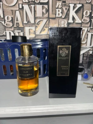 Mancera Tonka Cola EDP - Mancera Tonka Cola Eau de Parfum med elegant svart och guld förpackning. Flaskan är genomskinlig med guldfärgat lock och etikett, och innehåller en bärnstensfärgad vätska. Doften är känd för sina unika toner av tonkaböna och cola. Skulle säga ungefär 100/120 ml kvar.