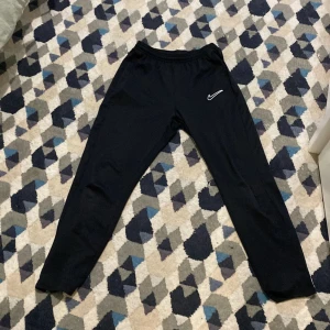 Svarta Nike Dri-Fit träningsbyxor - Svarta Nike träningsbyxor knappt använda. Jag säljer de för att de blev för små för mig väldigt snabbt, annars är den i fin och ren som i nytt skick inga hål och helt osliten. Det är storlek 158-170 den har 2 fickor med dragkedja. 