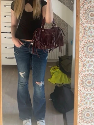 Blå bootcut jeans-Gina Tricot  - Säljer ett par blå bootcut jeans med slitningar och hål på benen. Jeansen har låg midja, klassisk femficksmodell från Gina tricot. Använd fåtal gånger! Strl 38/M