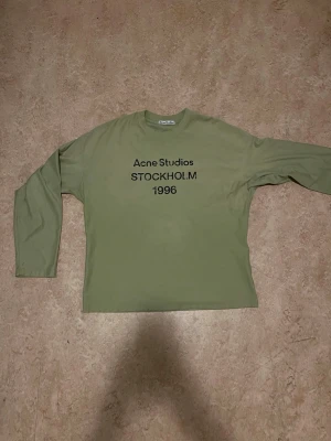 Grön långärmad topp Acne Studios - Snygg grön långärmad topp från Acne Studios med tryck 'STOCKHOLM 1996' på bröstet. Klassisk rund halsringning och relaxed fit. Perfekt för dig som gillar minimalistisk och stilren design.