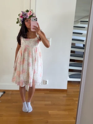 Blommig sommarklänning med volang - Söt kort blommig klänning i ljusa toner med volangdetaljer på axelbanden. Klänningen har en luftig passform och är ärmlös, perfekt för varma dagar. Färgerna går i vitt, rosa och orange. Lappen är bortklippt men skulle säga att den motsvarar xs