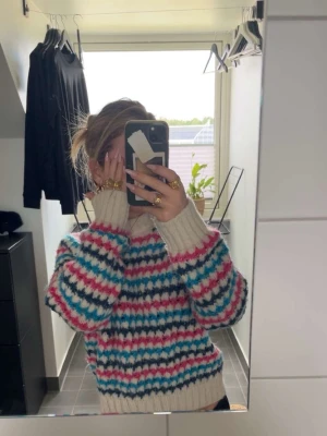 Färgglad stickad tröja med mönster - Säljer en mysig stickad tröja med breda ribbade muddar och rund hals. Tröjan har ett färgglatt zigzag-mönster i vitt, blått, svart och rosa. Perfekt för dig som gillar retrovibbar och vill ha något unikt i garderoben.