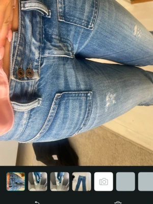 Blå bootcut jeans med slitna detaljer - Säljer ett par blå bootcut jeans med lätt slitna detaljer och rå kant vid benslut. Jeansen har klassisk femficksdesign och normal midja. Perfekta för en avslappnad och trendig look. 39 midja 78innerben