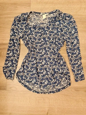 Blommig långärmad blus H&M XS - Söt blå blus med vitt blommönster och långa ärmar. Blusen har en figurnära passform med lätt rynk vid midjan och rundad nederkant. Tillverkad i ett tunt och mjukt material som känns skönt mot huden. Tunn och skön inför sommaren!