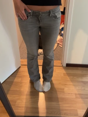 Grå bootcut jeans med låg midja - Säljer ett par gråa jeans med bootcut-modell och låg midja. Jeansen har klassiska fem fickor och silverfärgade knappar och nitar. Perfekta för dig som gillar en avslappnad men ändå trendig look.