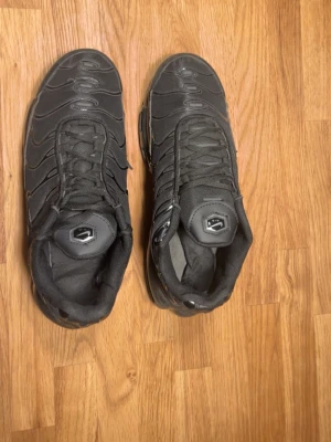 Svarta sneakers med synlig luftdämpning - Säljer ett par helsvarta sneakers med synlig luftdämpning i sulan och vågformade detaljer på ovandelen. Skorna har snörning och en sportig look med mesh och syntetmaterial. Perfekta för dig som gillar streetwear och vill ha bekväma skor till vardags.