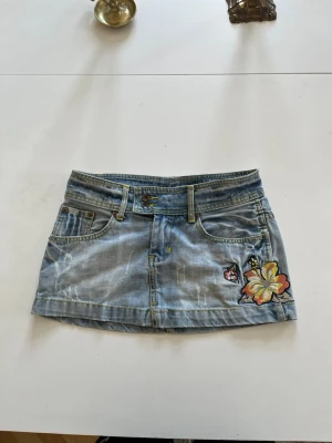 Ljusblå jeanskjol med broderade blommor - Ljusblå lågmidjad jeanskjol med broderade blommor på💞 Köpt second hand men inga defekter, skriv om du har någon fundering!