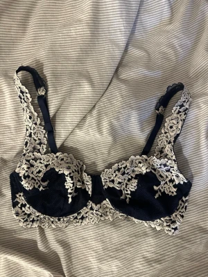 Mörkblå spets-bh med brodyr - Snygg mörkblå bh med vacker beige spets och broderade blommor. Bh:n har justerbara axelband och bygel för extra stöd. Materialet är en kombination av spets och mesh som ger en lyxig känsla och elegant look. Knappast använd🥰