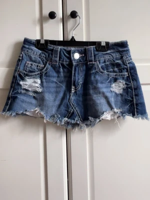 Blå jeanskjol med slitningar - Säljer en blå jeanskjol med slitna detaljer och fransig nederkant. Helt oanvänd men ingen prislapp kvar 