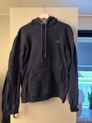 Les Deux Hoodie - Säljer en mörkblå hoodie med huva och dragsnören. Hoodien har en stor magficka framtill och ribbade muddar vid ärmar och nederkant. Liten patch på bröstet. Perfekt för chill dagar eller när du vill ha något bekvämt. Strl M
