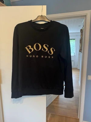 Svart sweatshirt från Hugo Boss - Tröja från boss. QR kod funkar bra att scanna, dock säljs inte tröjan längre hos boss. Storlek L men passar M bäst. Jag skulle säga till någon mellan 175-185.  Inga skador eller nått på tröjan, väldigt bra skick.