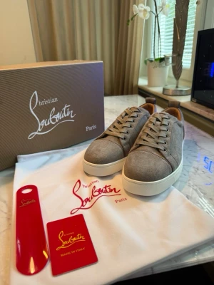 Gråa sneakers från Christian Louboutin - Snygga gråa sneakers från Christian Louboutin med ovandel i mocka och vita tjocka gummisulor. Skorna har rund tå, gråa skosnören och diskreta detaljer. Perfekta för dig som gillar stilrena och exklusiva sneakers.
