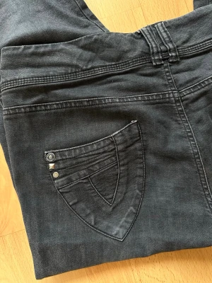Capribyxor-trekvartsjeans - Coola och unika trekvartsjeans i mörkblå tvätt. Modellen är en figurnära "Slim"-modell i caprilängd, perfekt för sommaren. Byxorna har fina detaljer så som  knappar vid bensluten, snygga sömmar och nitar på både fram- och bakfickorna som ger dem det lilla extra✨