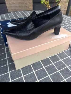Svarta spetsiga pumps i skinn - Stilrena svarta pumps med spetsig tå och låg klack. Skorna är tillverkade i slätt skinn och har en klassisk slip-in modell utan remmar. Perfekta för dig som gillar en elegant och tidlös look.