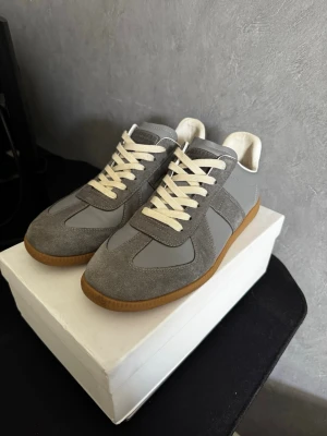 Grå Maison Margiela gats - Stilrena sneakers i grått från Maison Margiela med ovandel i mocka och läder, vita snören och klassisk gummisula. Snygg retrodesign som passar till många olika outfits. Perfekta för dig som gillar minimalistisk och tidlös stil.