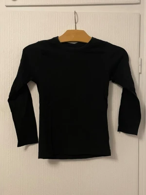 Svart långärmad baströja - En enkel svart långärmad topp i basmodell. Perfekt att ha som lager eller till vardagslooken. Mjuk och skön med rund halsringning och normal passform.