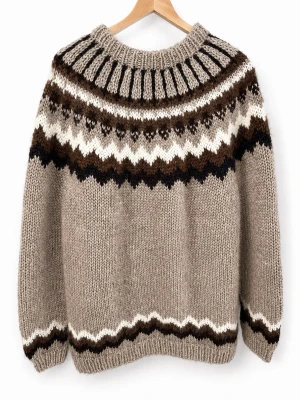 Beige islandströja med mönster - Stickad islandströja i beige med klassiskt mönster i brunt, svart och vitt runt oket. Tröjan har rund hals, långa ärmar och ribbstickade muddar. Tillverkad i tjock ull för extra värme och mysfaktor. Nypris: ca 400 Euros