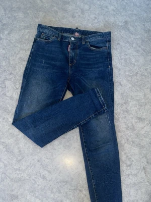 Mörkblå skinny jeans med slitningar - Säljer ett par mörkblå skinny jeans med lätt slitna detaljer och klassisk femficksmodell. Jeansen har normal midja, dragkedja och knapp framtill samt smal passform hela vägen ner. Perfekta till en avslappnad streetstyle-look.