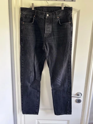 Zara Svarta raka jeans med hög midja - Säljer ett par svarta jeans med rak passform och hög midja. Jeansen har klassiska fem fickor och knappgylf. Materialet är denim i 100% bomull och färgen är tvättad svart för en cool vintagekänsla.