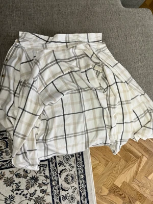Vit och beige rutig skjorta - Säljer en vit skjorta med beige och gråa rutor. Skjortan har klassisk krage, knappar framtill och långa ärmar med knapp vid manschetten. Perfekt för en avslappnad men ändå stilren look.