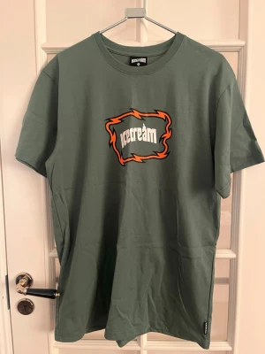 Grön Icecream t-shirt med tryck - Säljer en grön t-shirt från Icecream med ett stort tryck på bröstet i vitt och orange. T-shirten har rund hals och korta ärmar. Materialet är mjuk bomull och passformen är normal. Perfekt för dig som gillar streetwear och coola prints.