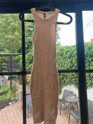 Beige ribbad ärmlös klänning - Säljer en beige ribbad klänning i stretchigt material. Klänningen är ärmlös, har en kroppsnära passform och är en kortklänning. Perfekt för varma dagar och enkel att styla med accessoarer.