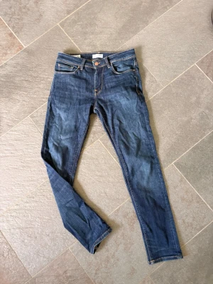 Mörkblå straight jeans från select home - Säljer ett par mörkblå jeans med klassisk femficksdesign och orangea sömmar. Jeansen har normal midja och smal passform hela vägen ner. Tillverkade i denim med stretch för extra komfort.