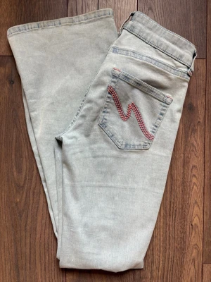 Ljusblå jeans från Nelly med rosa detalj - Ljusblå jeans från Nelly med klassisk femficksdesign och rosa zigzag-detalj på bakfickan. Jeansen har en utsväng  passform och rå kant nertill på ena benet. Tillverkade i mjukt denimtyg med subtila slitningar för en avslappnad look.