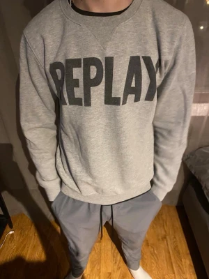Grå sweatshirt från Replay - Snygg grå sweatshirt från Replay med stor svart logga framtill. Tröjan har rund halsringning, långa ärmar och ribbade muddar vid ärmslut och nederkant. Perfekt för en avslappnad och trendig stil.