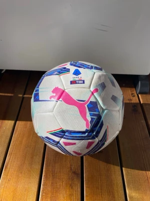 Puma Serie A fotboll - Säljer en officiell Serie A fotboll från Puma i vitt med blå, rosa och turkosa detaljer. Bollen har en stor rosa Puma-logga och Serie A TIM-märke. Perfekt för dig som älskar fotboll och vill ha en snygg boll att spela med.