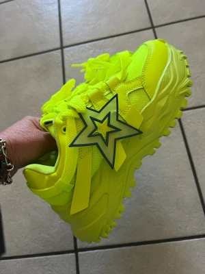 Neongula chunky sneakers med stjärndetalj - Säljer ett par riktigt feta sneakers i neon-gult med chunky sula och en stor stjärndetalj på sidan. Skorna har mesh och syntetmaterial för extra streetkänsla och breda snören. Perfekta för dig som vill sticka ut och maxa din outfit.