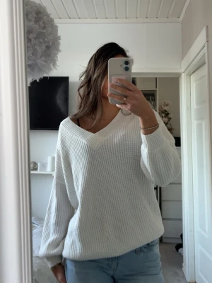 Vit stickad v-ringad tröja - Säljer en vit stickad tröja med v-ringning och avslappnad passform. Tröjan har långa ärmar och bred ribbad kant vid halsen. Tröjan har kommit till användning men inga synliga defekter.