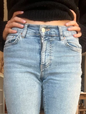 Ljusblå midwaist bootcut jeans - Säljer ett par ljusblå bootcut jeans med medelhög midja och klassisk femficksdesign. Jeansen har dragkedjegylf och knapp. Perfekta till en avslappnad och trendig look.