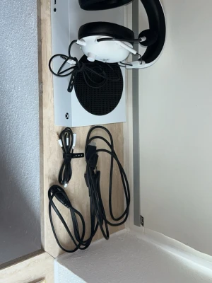 Xbox Series S spelkonsol med tillbehör - Säljer en vit Xbox Series S spelkonsol med tillhörande kablar och ett par vita gaminghörlurar. Konsolen har en kompakt, rektangulär form med en stor svart cirkulär ventil på ovansidan. Perfekt för dig som vill spela nya generationens spel.  Hej, jag säljer mitt Xbox Series S med Ett splitter nytt headset och kablar till headsetet och kablarna till Xbox.  Allt fungerar precis som det ska och har aldrig tagit en skada.