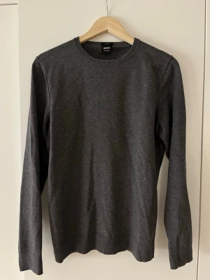 Mörkgrå tröja från Hugo Boss - Mörkgrå slim fit tröja från Hugo Boss med rund halsringning och långa ärmar. Enkel och stilren design i mjukt material, perfekt för en clean och modern look.