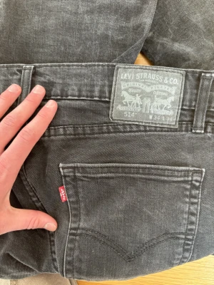 Svarta Levi's 514 straight jeans - Säljer ett par svarta Levi's 514 straight jeans med klassisk femficksdesign och röd Levi's-tag på bakfickan. Jeansen har normal midja och raka ben, tillverkade i slitstarkt bomullsmaterial. Perfekta för en avslappnad och tidlös stil.