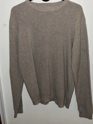 Beige stickad tröja från Teorema - En enkel och stilren beige stickad tröja från Teorema. Tröjan har rund halsringning, långa ärmar och är tillverkad i ett mjukt, tunt stickat material. Perfekt för lager på lager och passar till det mesta i garderoben.