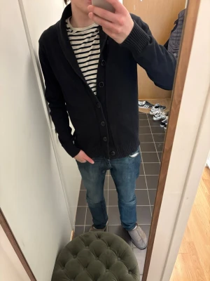 Svart kofta med sjalkrage - Säljer en svart kofta från jack and Jones med sjalkrage och knäppning framtill. Koftan har ribbade muddar vid ärmslut och nederkant, samt en stilren och enkel design som passar till det mesta. Perfekt för lager på lager och chill stil.