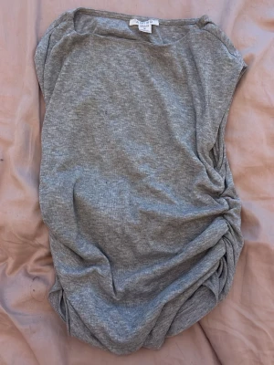 Grå ärmlös topp från Amisu - Snygg grå ärmlös topp från Amisu i mjuk bomullsblandning. Toppen har en enkel, rak passform med lätt rynkade detaljer på ena sidan som ger en cool twist. Perfekt att styla med jeans eller kjol för en avslappnad look.