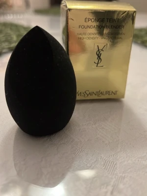 Svart beautyblender från Yves Saint Laurent - En svart, droppformad beautyblender från Yves Saint Laurent. Perfekt för att applicera foundation jämnt och smidigt. Tillverkad i mjukt, högdensitetsmaterial som är antibakteriellt. Kommer i lyxig guldförpackning.