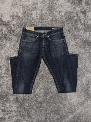 Mörkblå jeans från Dondup  - Snygga mörkblå jeans från Dondup med klassisk femficksdesign och diskreta slitningar. Jeansen har raka ben och kontrastsömmar, samt detaljerade bakfickor med Nudie Jeans signatursöm. Perfekta för en trendig och avslappnad stil.
