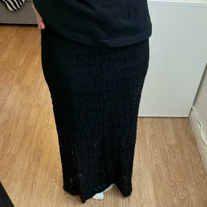 Svart långkjol i spets - Snygg svart långkjol med spetsdetaljer och diskret mönster. Kjolen har en rak passform och är perfekt för dig som gillar en elegant och stilren look. Materialet är mjukt och följsamt, vilket gör den bekväm att bära hela dagen.