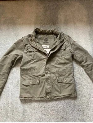 Olivgrön fieldjacka från Brandit - Säljer en riktigt fet olivgrön fieldjacka från Brandit med flera fickor framtill, både med knapp och lock. Jackan har dragkedja och knappar framtill. Vid funderingar, fråga på! 