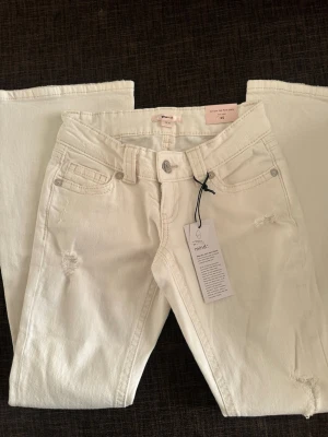 Gina Tricot 14+ low rise petite flare jeans – XS - Helt nya vita Gina Tricot 14+ jeans med alla prislappar kvar. Storlek XS Petite.🤍  Mycket låg midja (low rise) i petite-modell, perfekt för kortare längd. Flare/utsvängda ben och en riktig Y2K-passform. Vita jeans med hål/ripped detaljer och broderade bakfickor. Låg stretch som ger mer klassisk denimkänsla. Framfickor och dragkedjegylf.  Material: 99 % bomull 1 % elastan