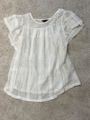 Vit spetsblus med volangärm - Säljer en luftig vit blus i spets med fina virkade detaljer och volangärmar. Blusen har rund halsringning och är lätt transparent, perfekt för lager på lager. Passformen är normal och materialet känns mjukt och bekvämt.