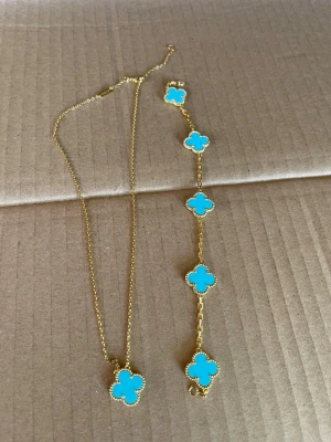 Guldpläterad halsband och armband  med turkos fyrklöver - 18k guldpläterad, hög kvalitet vattentålig Snyggt halsband och armband  i guldton med en turkos fyrklöverformad berlock. Kedjan är tunn och elegant, och berlocken har en dekorativ kant. Perfekt för dig som vill ha en färgklick till din outfit.