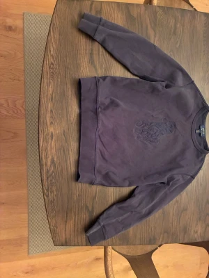 Lila sweatshirt från Ralph Lauren - Säljer en lila sweatshirt från Ralph Lauren med det klassiska stora broderade polospelar-motivet på bröstet. Tröjan har rund halsringning och är tillverkad i mjukt bomullsmaterial. Perfekt för en avslappnad och stilren look. 152 cm